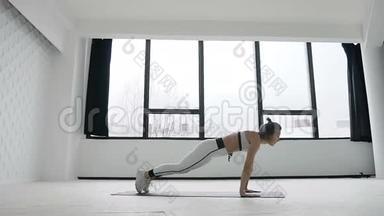 年轻的健身金发女子在健身房附近大窗户锻炼，在上午的运动，训练锻炼。 她穿着